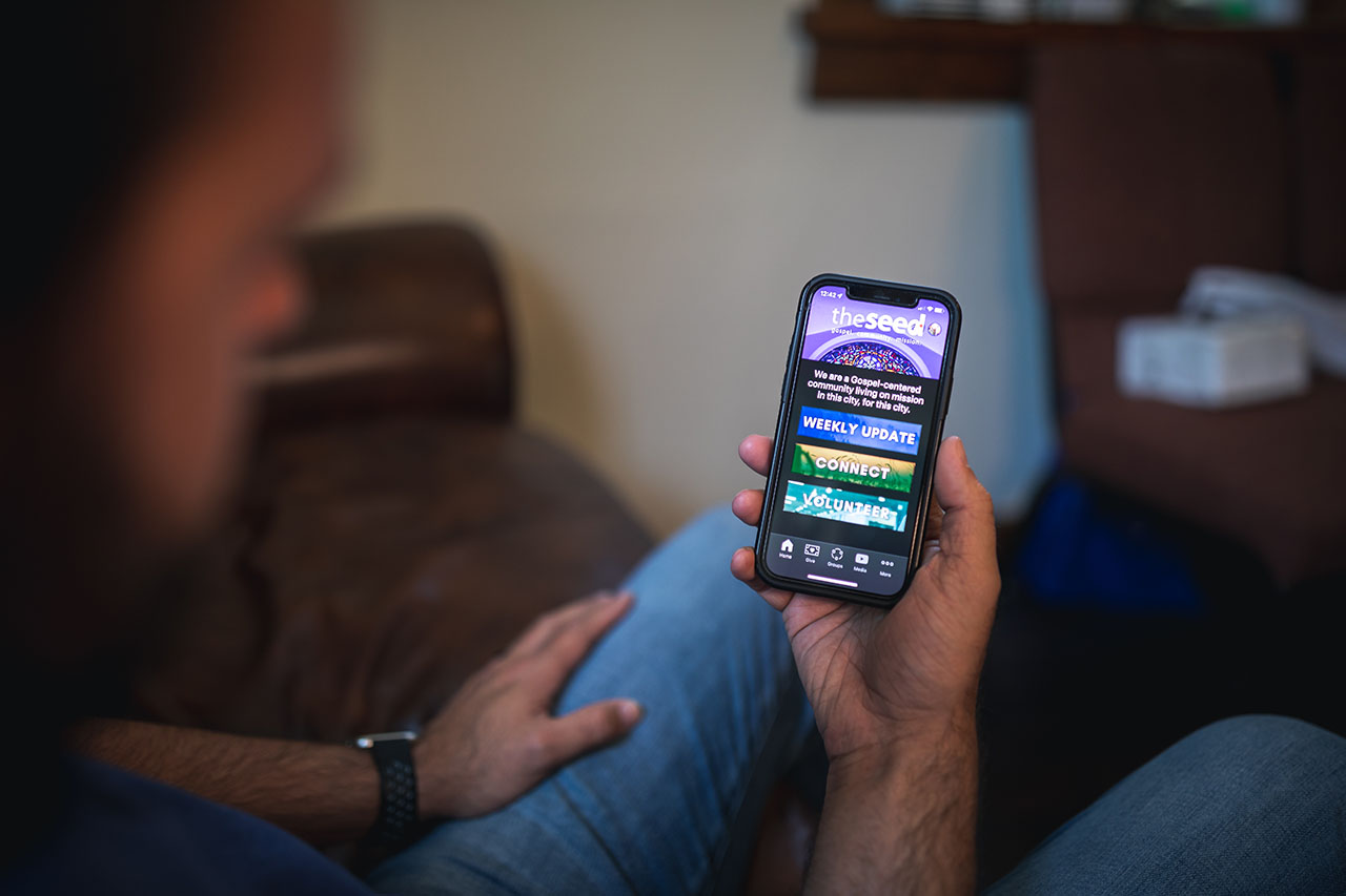 A man holds an iPhone showing the Seed on the Church Center app.